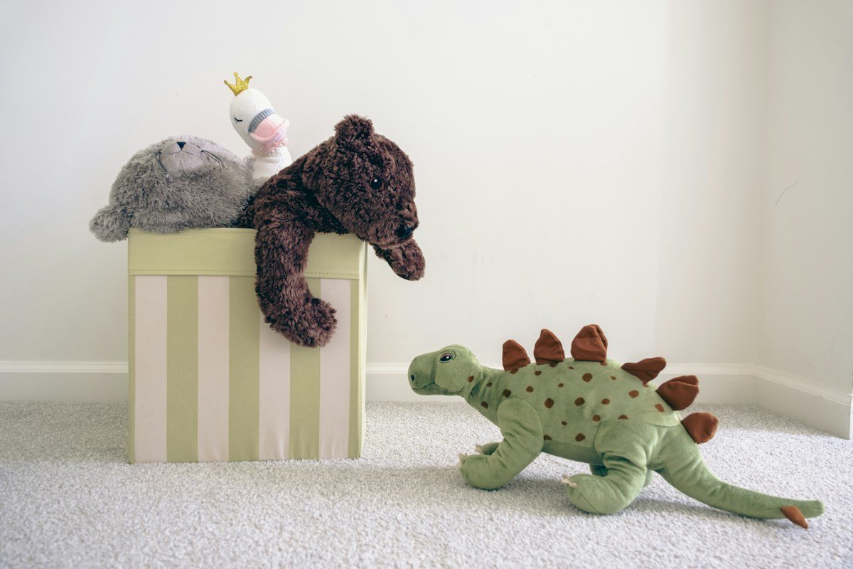 Kiste mit Stofftieren, daneben ein Plüsch-Dinosaurier